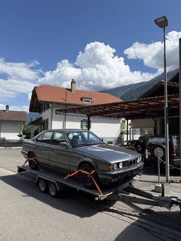 Grauer BMW E34 auf dem Anhänger vor der Werkstatt
